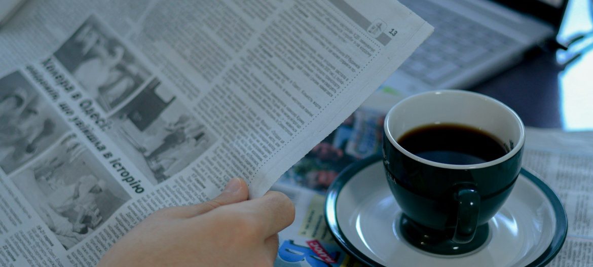 a person reading a newspaper with a cup of coffee