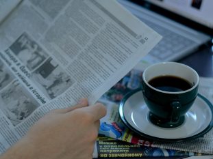 a person reading a newspaper with a cup of coffee