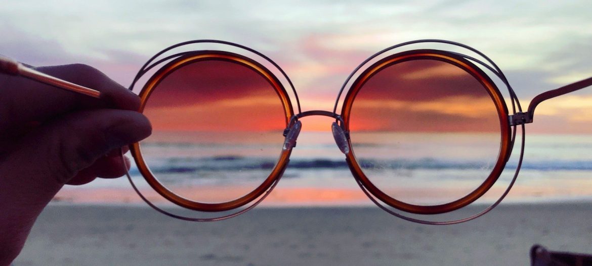 a person holding up a pair of sunglasses on the beach