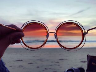 a person holding up a pair of sunglasses on the beach