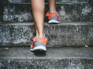 person wearing orange and gray Nike shoes walking on gray concrete stairs